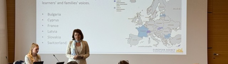 A person presenting at the front of a room full of audience members sitting on chairs. The screen behind the speaker says 'TCCA cluster 3 objective and countries'