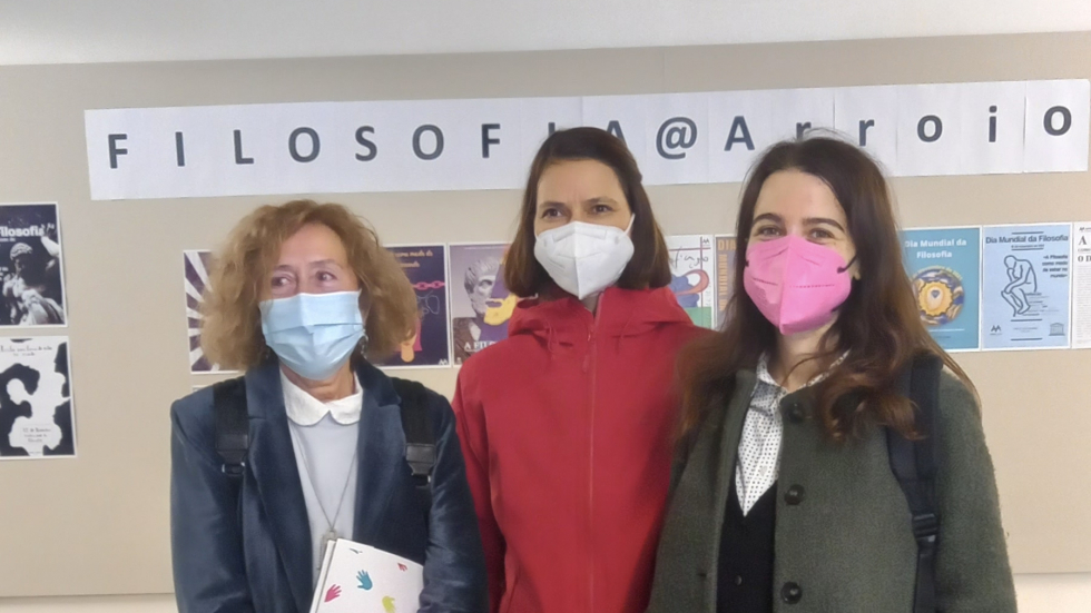 Three people wearing masks stand in front of a school display board