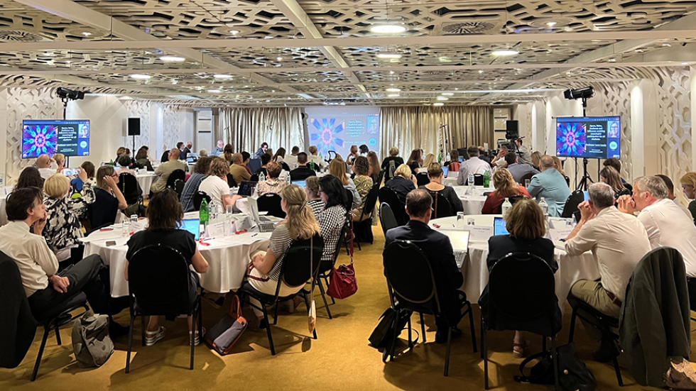 Participants at the bi-annual meeting sit around round tables and watch a presentation on a screen at the front of the room