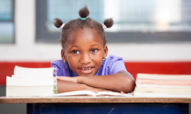 A smiling child sitting at a desk with books piled to each side