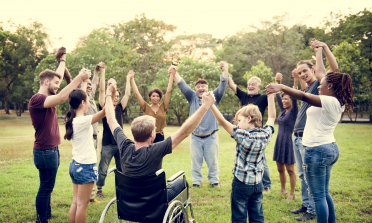 A group of people of different ages stand in a circle holding hands