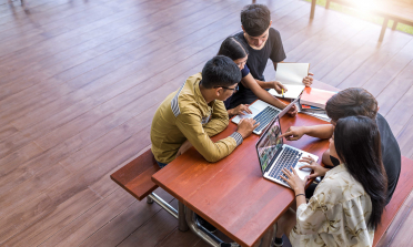 Four teenage learners sit around a table working on their laptops