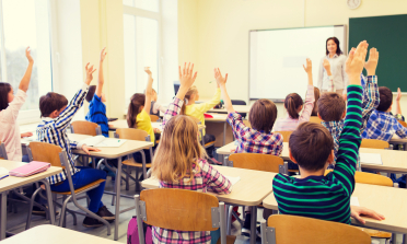 Children in a classroom with their hands in the air