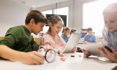 Three children look at a tablet screen in a classroom