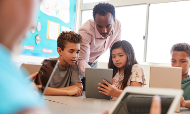 A teacher and two learners look at a tablet screen