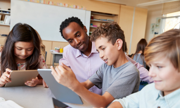 A child shows a teacher his work on a tablet