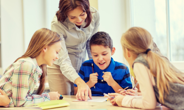 A teacher congratulates a boy on his work as his friends watch