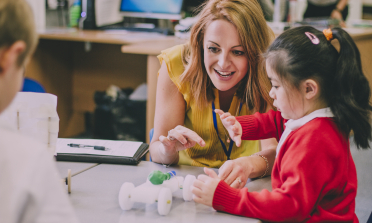 A teacher encourages a child who is experimenting with a model car with a balloon attached