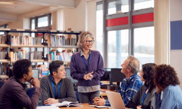 A group of teachers sit around a table with bookshelves behind them