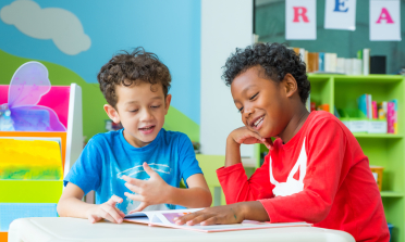 Two children smile while reading a book together