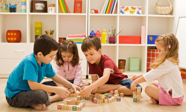 Four children sit on the floor playing with building blocks