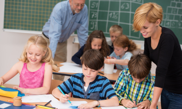 Two adults help learners who are working at desks in a classroom