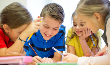 Four children smiling and writing together around a table