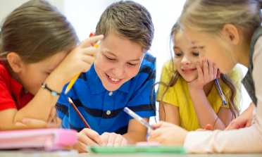 Four children smiling and writing together around a table