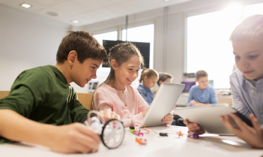 Two children look at a computer screen, one holding a magnifying glass