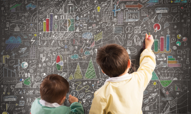 Two children draw on a blackboard covered in graphs and notes