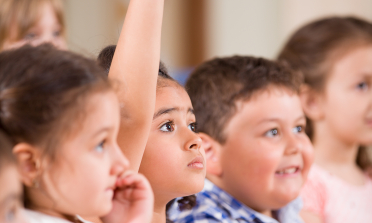 A group of children sitting together, a girl has her hand in the air