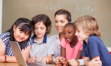 four children and their teacher look at a laptop screen