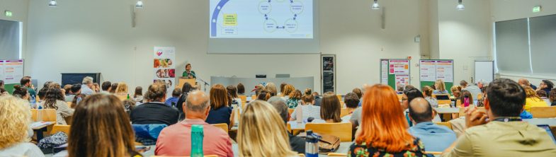 People listening to a presentation in a large room with a screen at the front