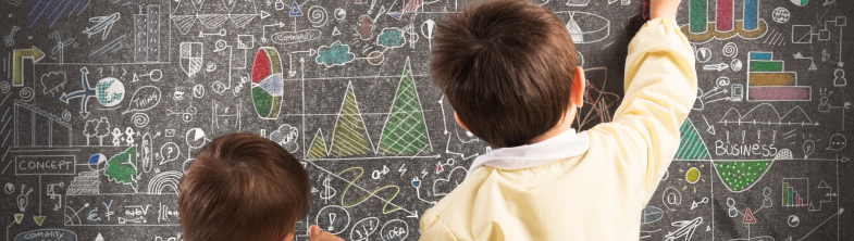 Two children write on a chalkboard that is full of charts and diagrams