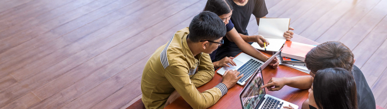 Four teenage learners sit around a table working on their laptops