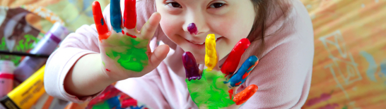 A girl smiles with her hands covered in brightly coloured paint