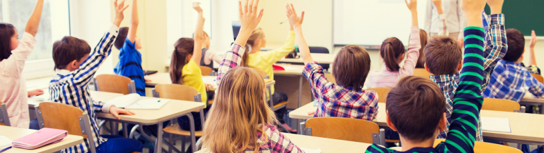 Children in a classroom with their hands in the air