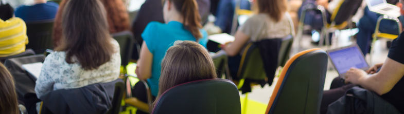 People in a conference room listening to someone speaking at the front