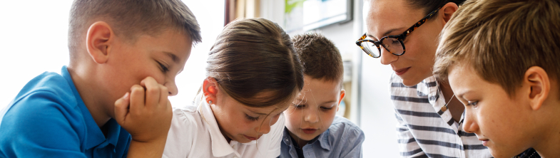 Four children and their teacher look at a workbook together