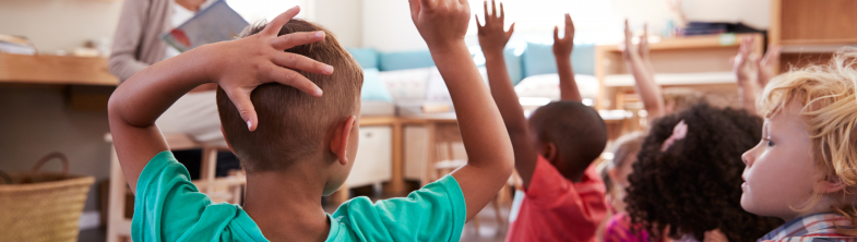 Children with their hands up in the classroom