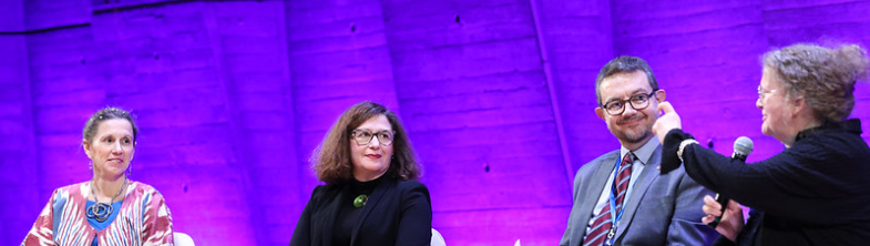 Amanda Watkins speaking on stage, alongside three other panelists © UNESCO/Marie ETCHEGOYEN