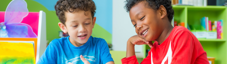 Two children smile while reading a book together