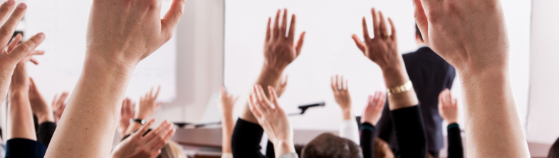 Learners in a classroom with their hands in the air