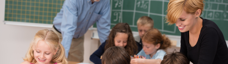 Two adults help learners who are working at desks in a classroom