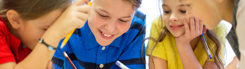 Four children smiling and writing together around a table