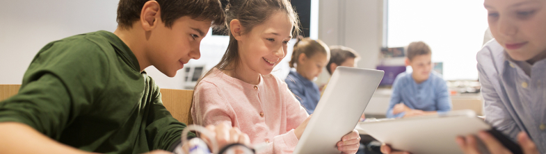 Two children look at a computer screen, one holding a magnifying glass