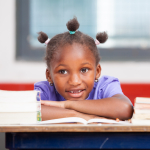A smiling child sitting at a desk with books piled to each side