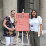 Two people stand either side of a sign that reads 'ECER 2025 check in'