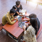 Four teenage learners sit around a table working on their laptops