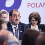 João Costa speaking in front of a sign saying Poland 25