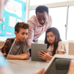 A teacher and two learners look at a tablet screen