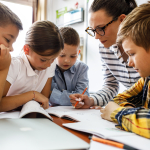 Four children sit with their teacher and read their work