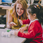 A teacher encourages a child who is experimenting with a model car with a balloon attached