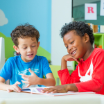 Two children smile while reading a book together