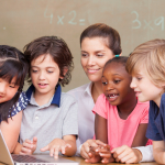 four children and their teacher look at a laptop screen