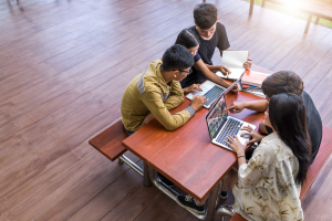 Four teenage learners sit around a table working on their laptops