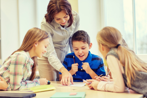 A teacher congratulates a boy on his work as his friends watch